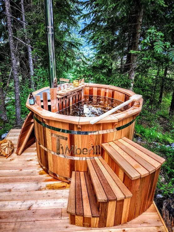 Types of Wood for Hot Tubs & Outdoor Saunas 4 Round TimberIN hot tub made from reddish brown western red cedar with timber steps on a wooded terrace