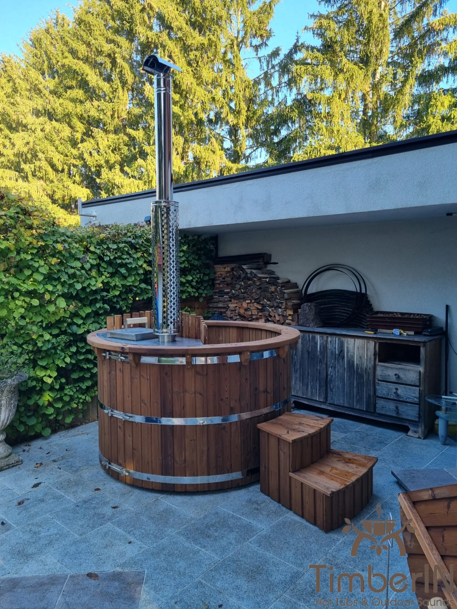 Round solid-wood TimberIN hot tub made from dark brown Thermowood with visible vertical grain and wooden steps