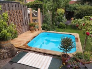 TimberIN Nordic Square wood-fired hot tub, with a timber or stone privacy fence, surrounded by garden planting, on a timber deck, in a landscaped garden