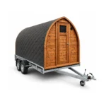 TimberIN Nordic Mobile Sauna Pod™ – arched mobile sauna pod with timber front, solid entrance door, black shingle shell and single-axle trailer on a white background.