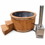 4 Person Hot Tubs 7 TimberIN Nordic External Comfort round hot tub with grey liner, thermowood cladding, wooden steps and separate stainless-steel wood stove with chimney on a white background.