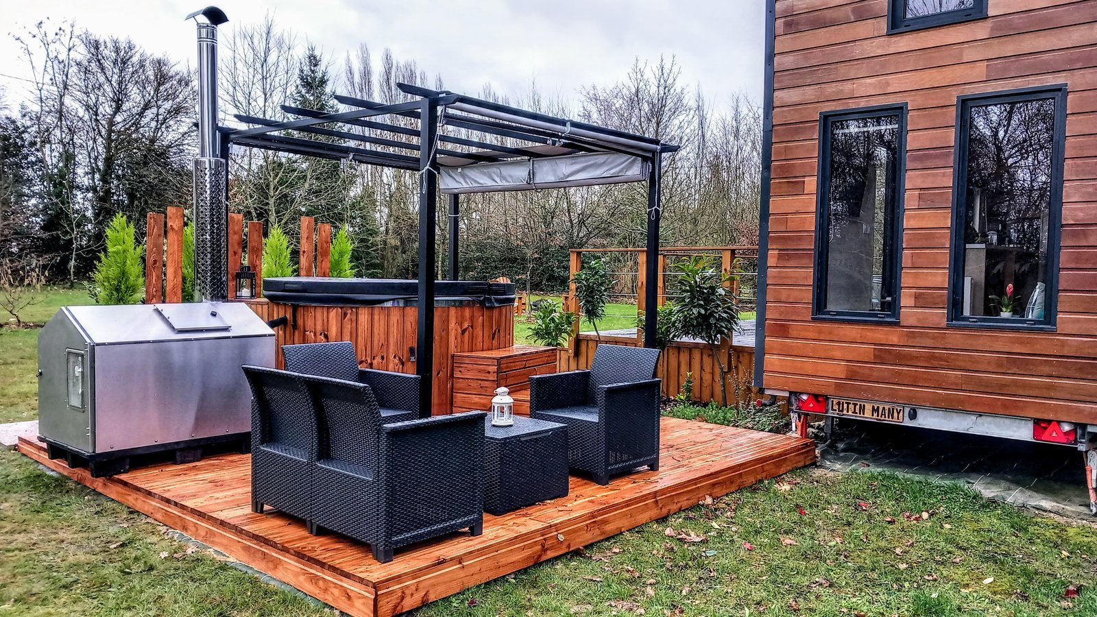 Covered timber-clad hot tub with a separate metal stove beside a deck and seating area