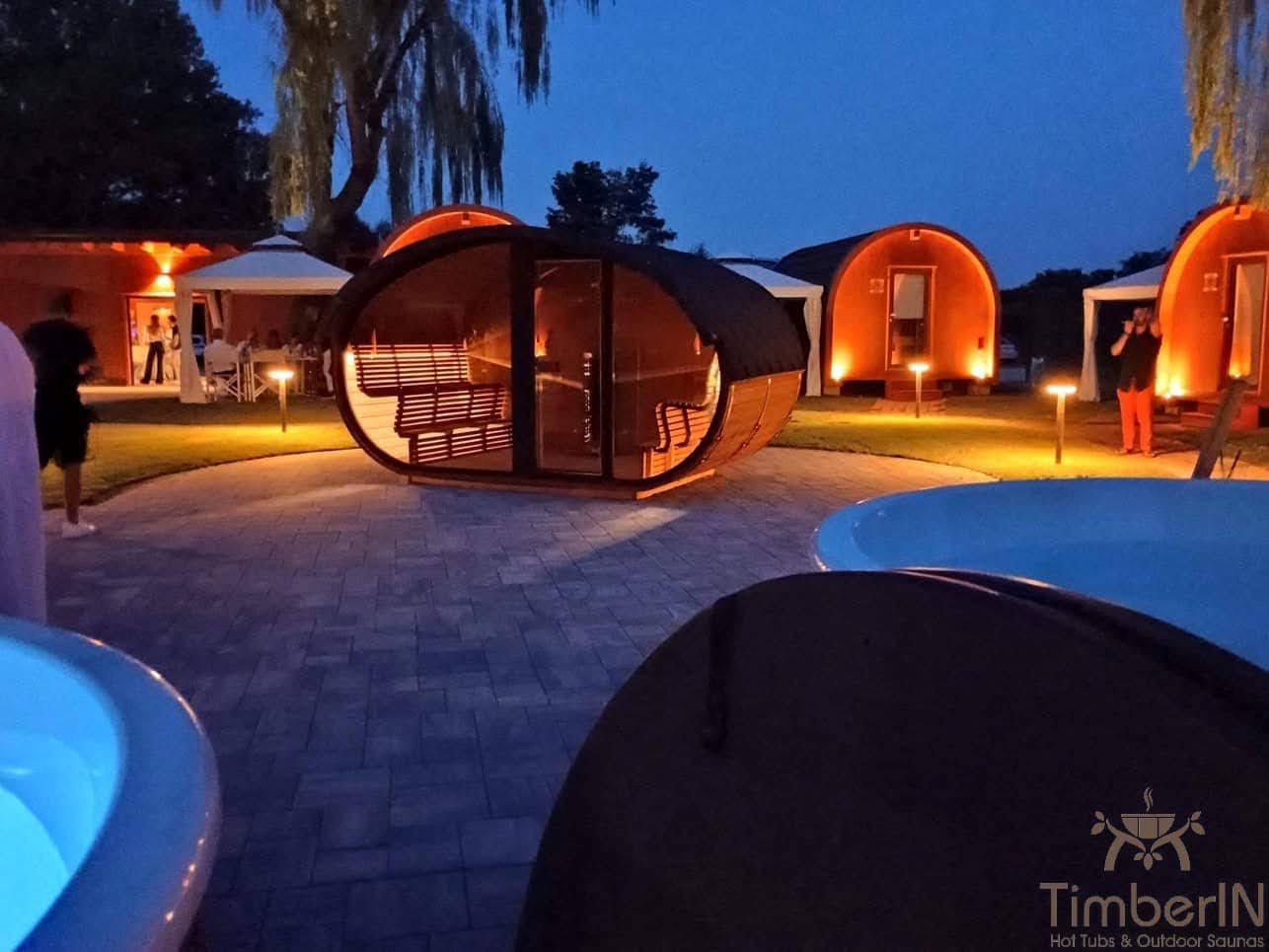 Barrel 1 Round timber sauna with a glazed front and visible benches in an illuminated outdoor display