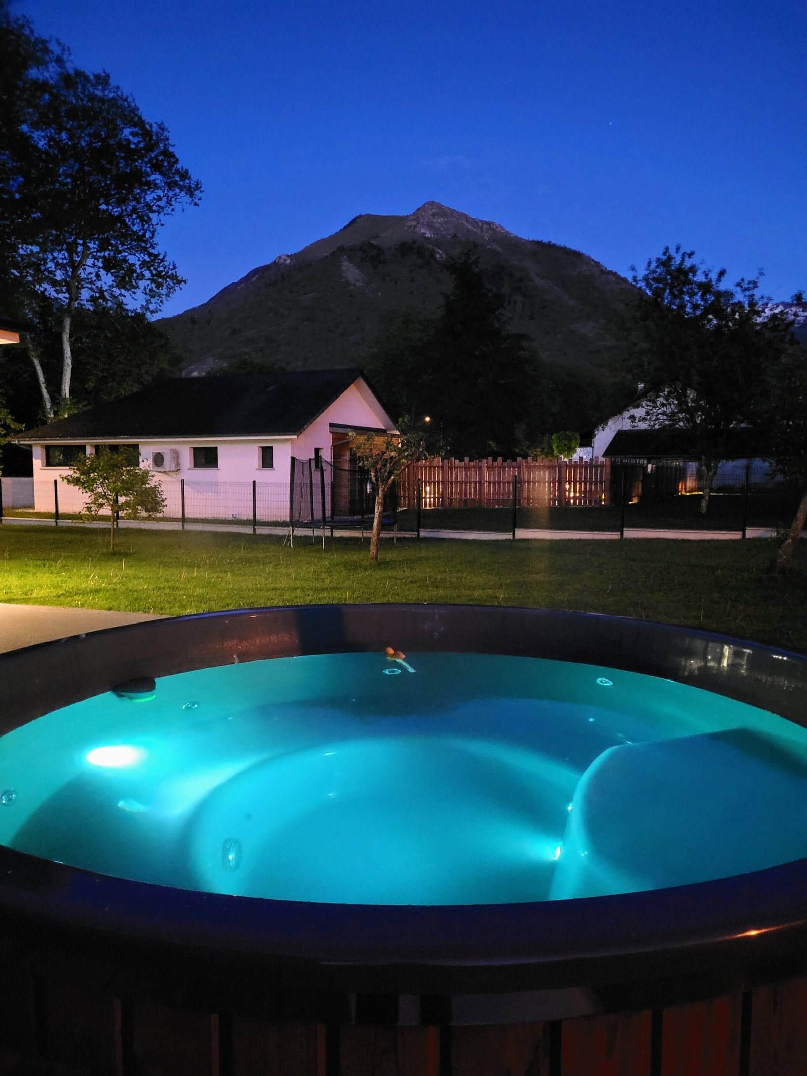 Round hot tub with illuminated blue water in a garden at dusk
