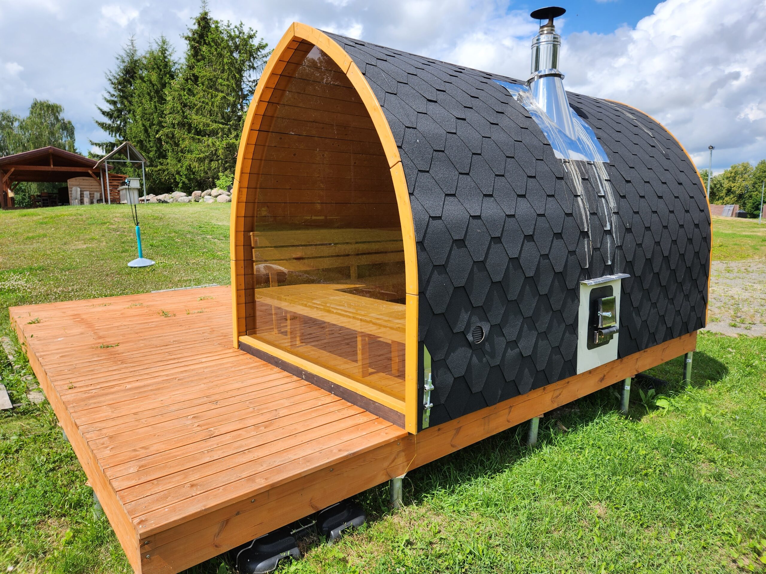Traditional - Finnish 1 Glass-front pod sauna with timber benches, dark shingle roof, outside firebox and chimney on a wooden deck