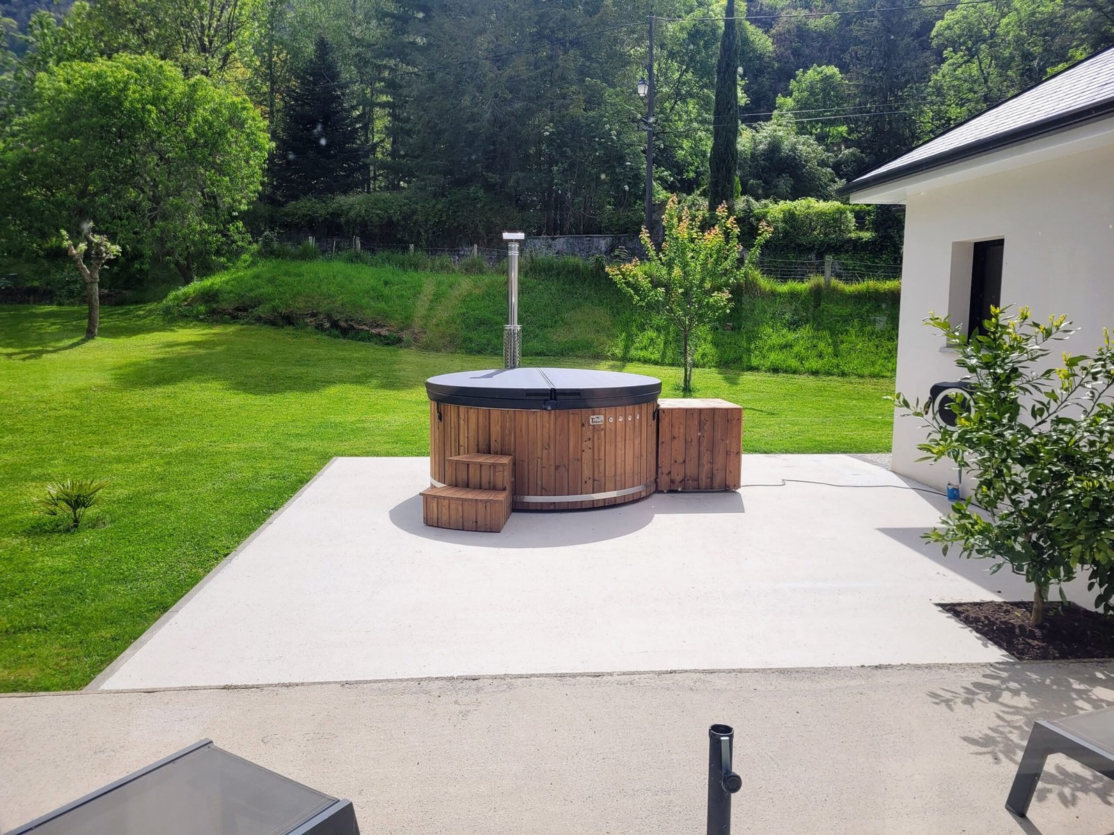 Family Hot Tubs 1 Covered round timber-clad hot tub with wooden steps, a side equipment enclosure and a metal flue on a garden terrace
