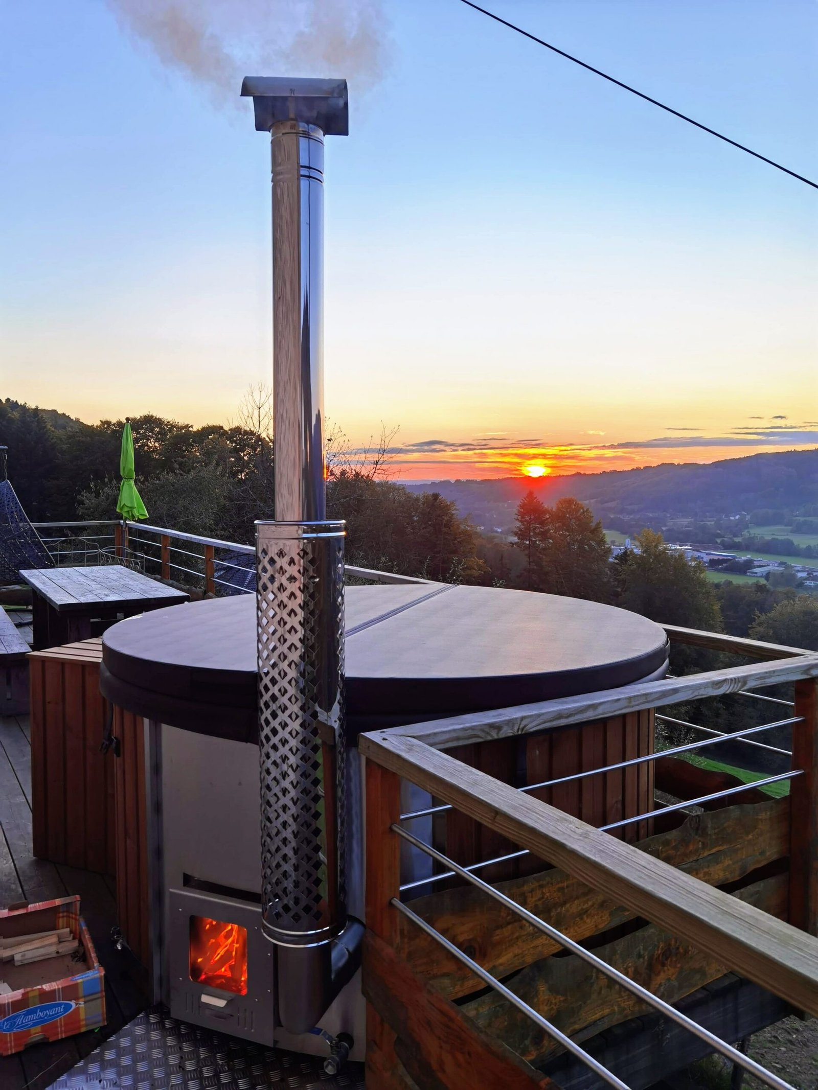 Ireland 1 Metal external heater with a glazed door and guarded flue beside a covered round timber hot tub at sunset