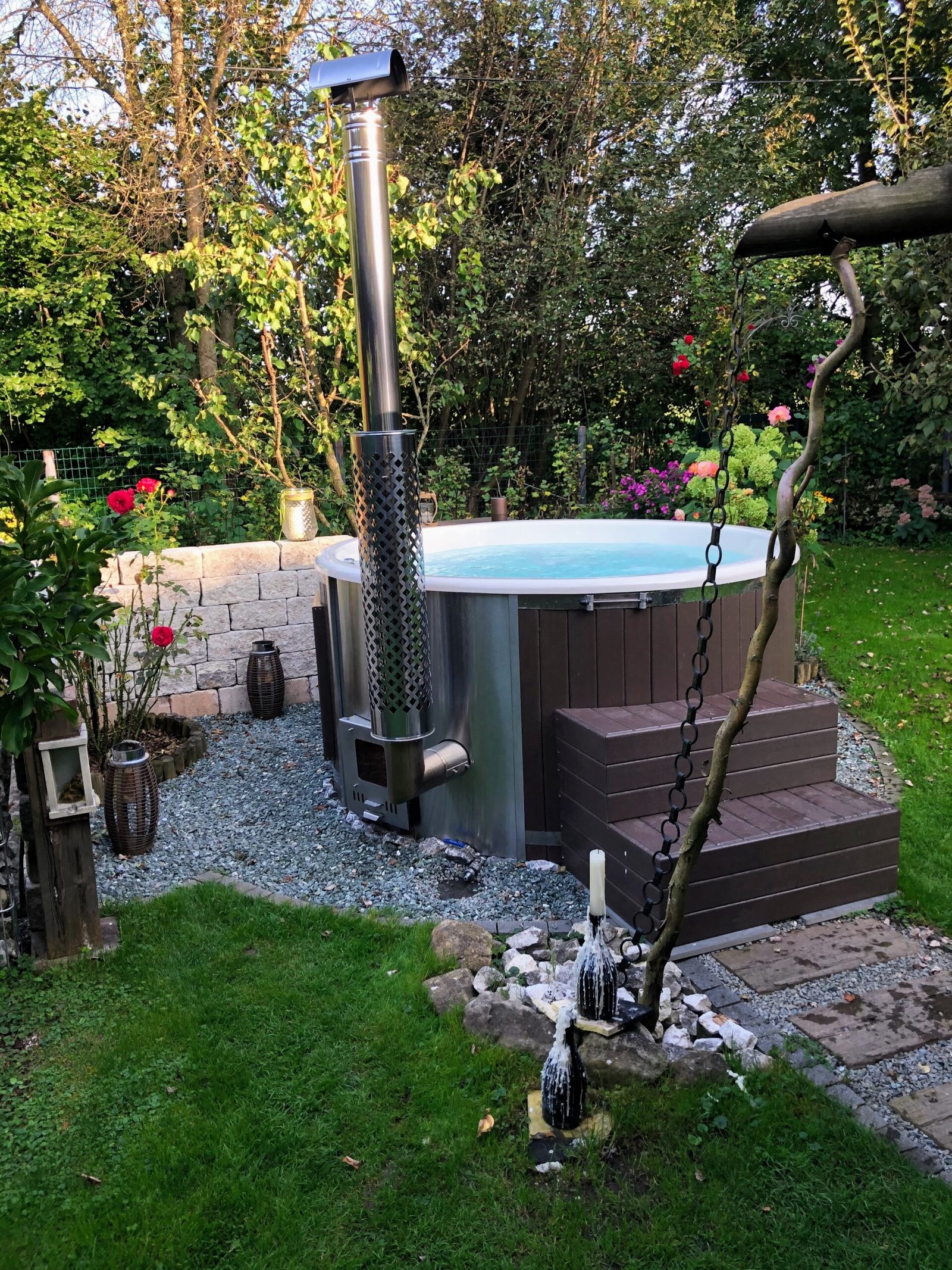 DIY Wood Fired Hot Tub 1 Timber-clad hot tub with a white liner, chimney guard and wooden steps in a planted gravel garden