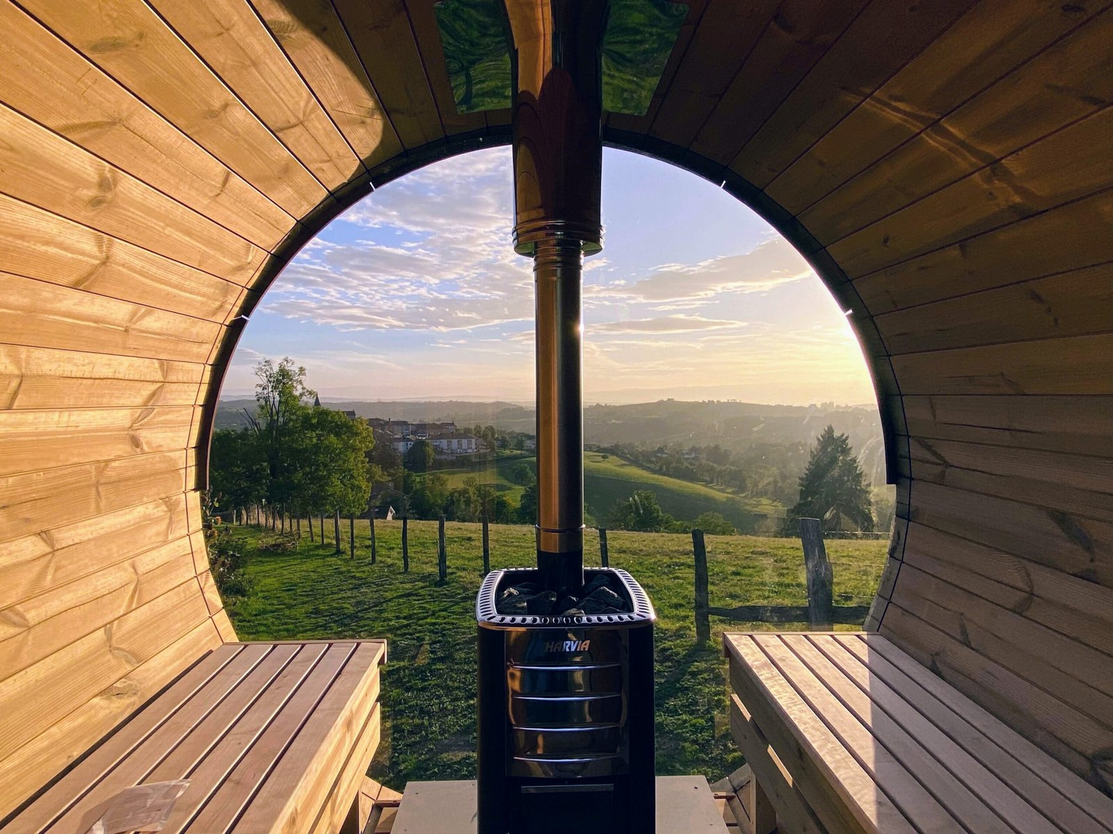 Cold plunge combo 1 Curved timber sauna interior with opposing benches and a stone-filled wood stove in front of a panoramic window