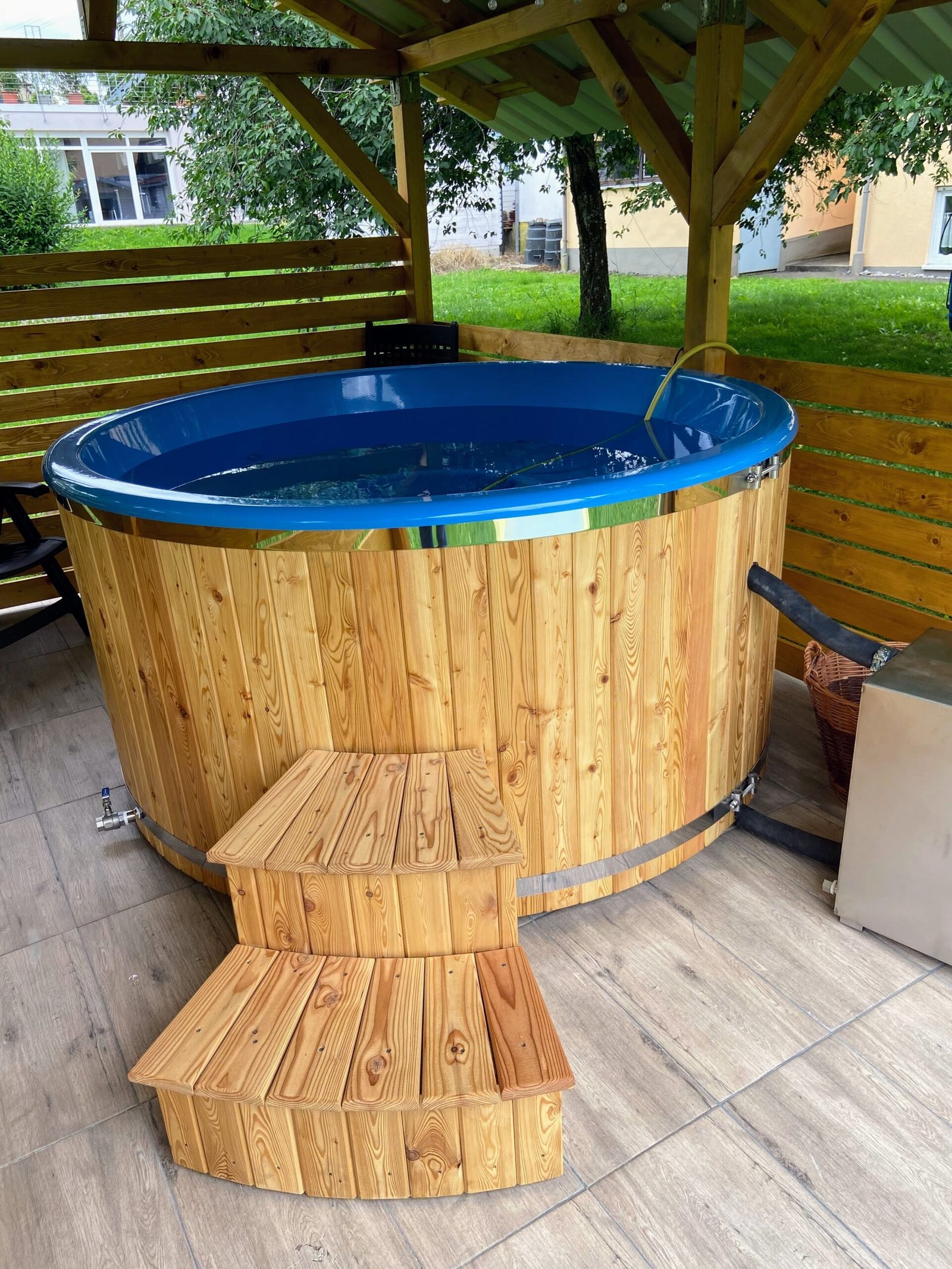 Second Hand Wood Fired Hot Tubs 1 Filled blue-lined hot tub with timber cladding, retaining bands, wooden steps and visible drain and side connection