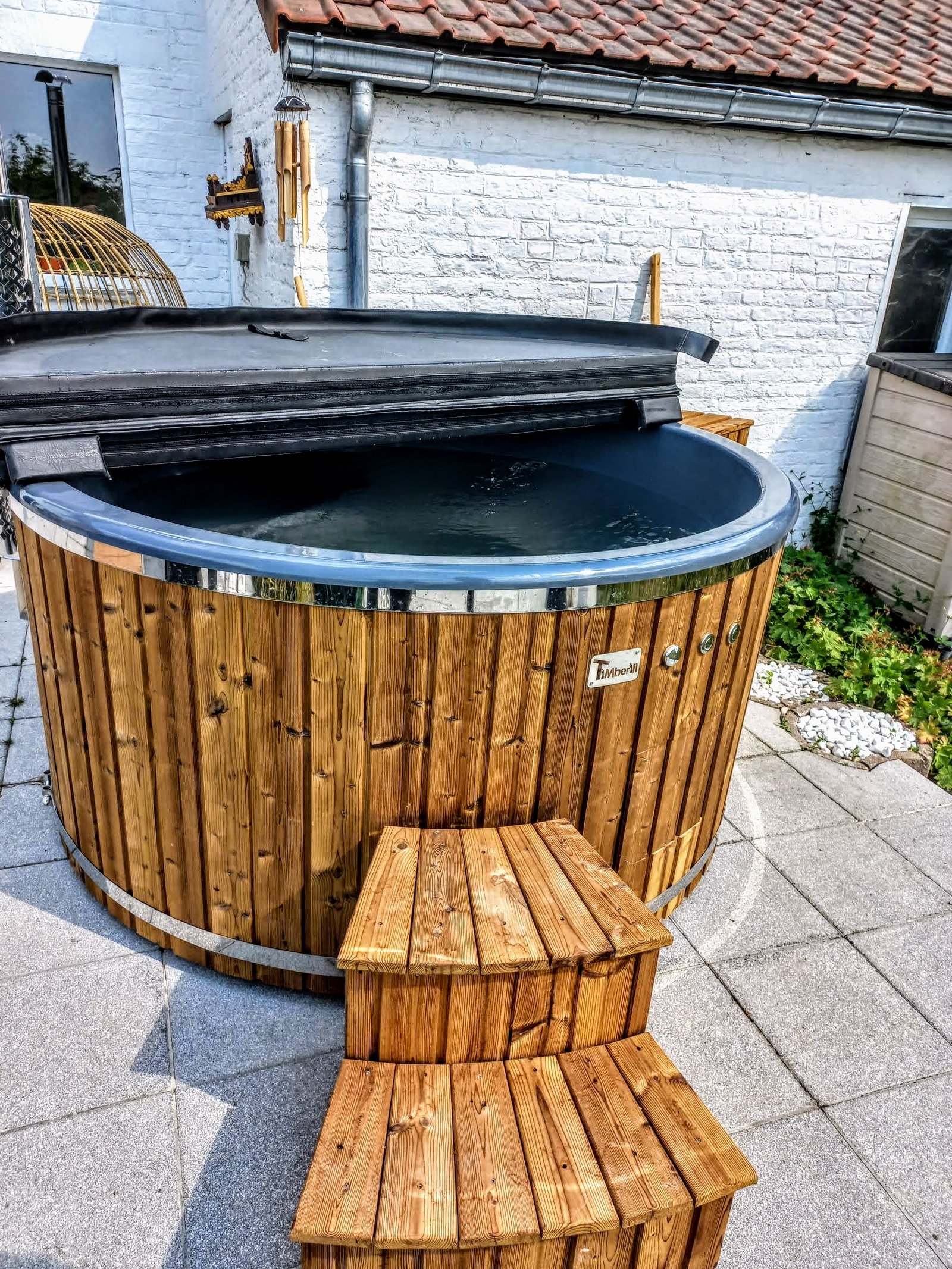 Hot Tub, Sauna and Outdoor Wellness Accessories 1 Round timber-clad hot tub with a blue liner, folded dark cover and two-level timber step on paving