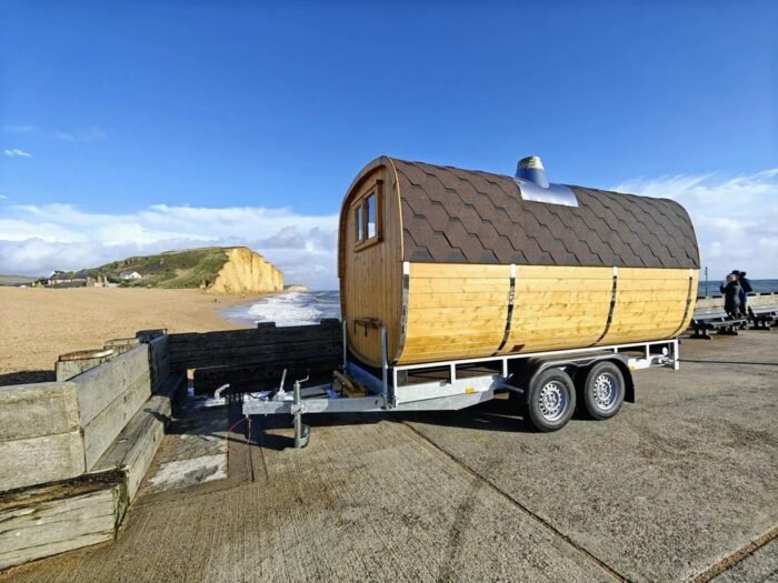 Barrel sauna on a twin-axle trailer beside the coast