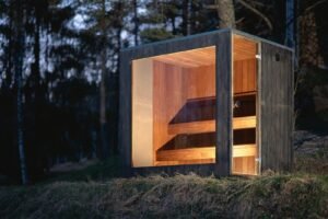 TimberIN Nordic Cube outdoor sauna with lit glass front at dusk